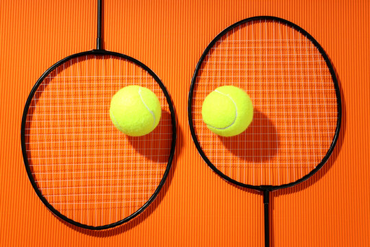 Badminton rackets and tennis balls on textured orange background