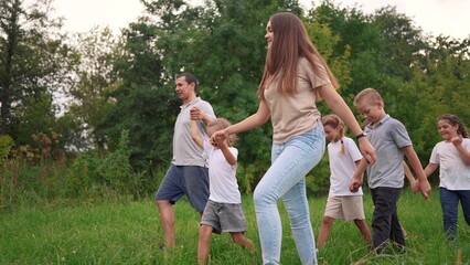 Fototapeta premium family walking on the grass in the park and holding hands. happy family childhood dream concept. a large family walks across the clearing and talks to each lifestyle other. outdoor nature walk