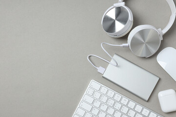 Powerbank, headphones and keyboard on gray background, space for text