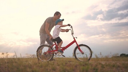 dad teaches son to ride a bike. happy family kid dream concept. the boy sat on bicycle for the first time, his father teaches boy to ride a bicycle. dog runs with lifestyle family, fun family pastime