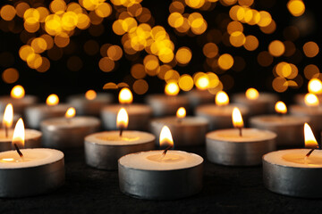 Fototapeta na wymiar Burning small candles on black background, close up