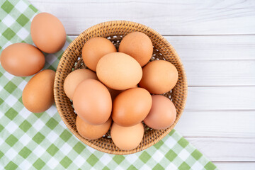 The Fresh eggs in a wooden weave basket and tablecloth on wooden background.