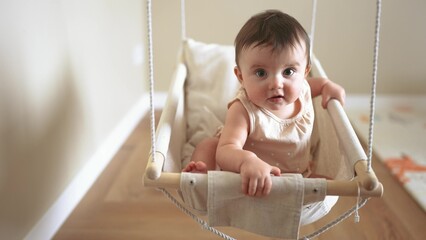 baby on a swing. happy family kid dream concept baby girl swinging on a swing at home indoors 8 months old. baby brunette plays at home swings lifestyle happy