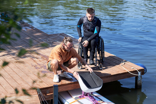 Portrait of senior water sports instructor preparing adaptive wakeboarding equipment for man with disability outdoors