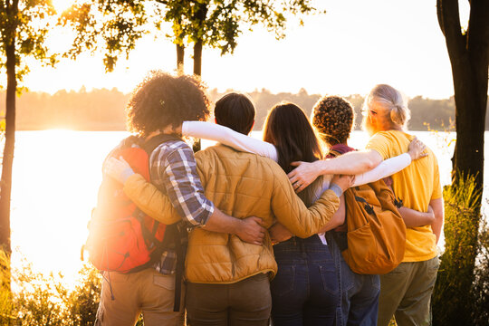 Experience the beauty of connection and nature's splendor in this heartwarming image. Young people with backpacks stand close, sharing an embrace while admiring the breathtaking sunset view over the