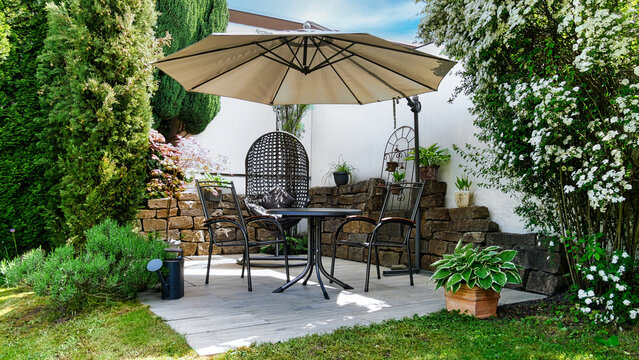 Gartenterrasse mit H&auml;ngesessel, Sonnenschirm und Sitzm&ouml;bel in einer Gartenecke mit S&auml;ulen-Faulbaum und umgeben von Pflanzen und Zypressen	