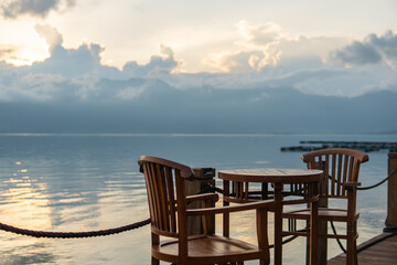 Fototapeta na wymiar Sunset view in Maninjau Lake with chair and cafe table for relaxing. Beautiful landscape in West Sumatra, Indonesia. Evening sun, clouds, and mountains.