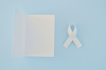 White ribbon as a symbol of peace and white paper on a blue background. World Day of Peace. Day Of...