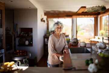 Smiling middle aged woman staying in the kitchen at home, single mature senior in living room	