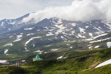 Fototapeta premium View of the hotel in the mountain valley and the volcano. Summer mountain landscape. Travel and tourism on the Kamchatka Peninsula. Nature of Siberia and the Russian Far East. Kamchatka Krai, Russia.
