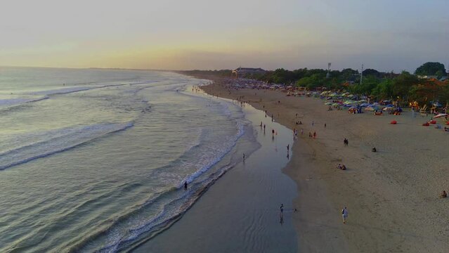 The bustling atmosphere of Legian Beach, Kuta, Bali, with the view of the trees and hotels during a crowded day, captured from the air using a drone. Aerial Video.