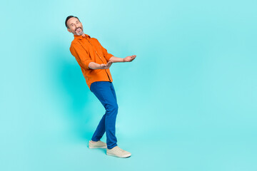 Full lenght photo of positive man dressed orange shirt holding arms empty space isolated turquoise color background