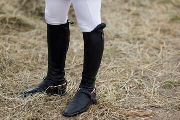 Female legs in black leather boots close up rider jockey standing at stable