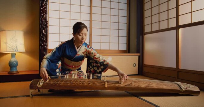 Portrait of a Talented Female Playing Koto Plucked String Instrument in Traditional Japanese Home. Musician Wearing a Blue Kimono, Practicing to Play Historic Music Before a Concert