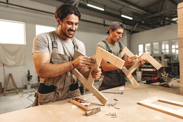 Two young men carpenters making furniture in warehouse of wood factory