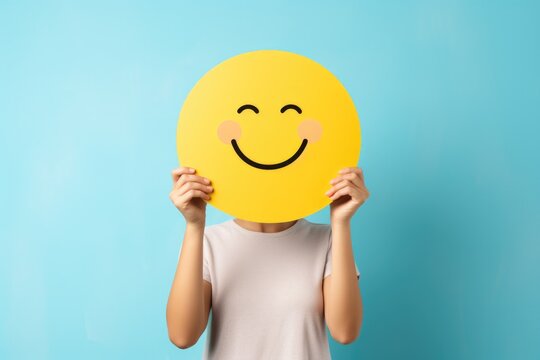 a woman holding up a yellow smiley face mask