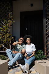 Fototapeta premium smiling african american man with coffee pointing at boxes near girlfriend on porch of new house