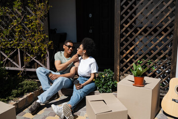 positive african american couple with coffee to go sitting near carton boxes and new house
