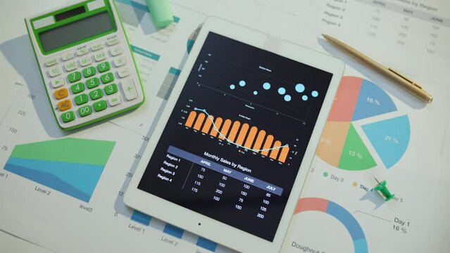 tablet pc, calculator, documents and graphs at desk.
