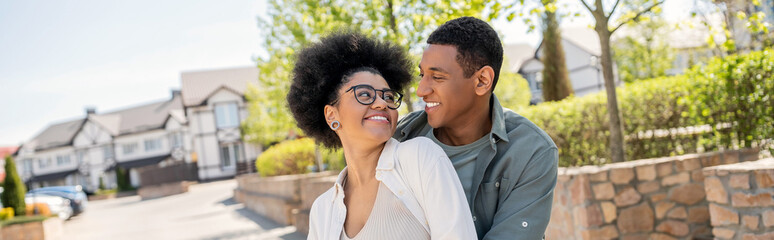 Fototapeta premium positive african american couple looking at each other on urban street in summer, banner