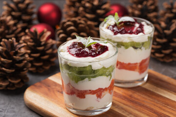 Dessert of cottage cheese cream, orange, kiwi, decorated with mint in glasses on dark table. Vegetarian organic dessert. Christmas and New Year's composition with red Christmas balls, pine cones.