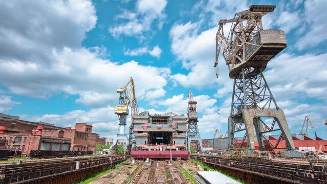 The construction of a large ship on a shipyard with cranes timelapse. A fragment of the case in the workshop of the plant. Metal frame during assembly front view. Cloudy sky