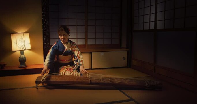 Talented Female Playing Koto Stringed Instrument in Traditional Dark Japanese Home with Lamp. Musician Wearing a Blue Kimono, Practicing to Play Historic Music Before a Performance