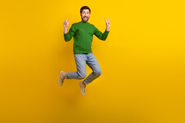 Fototapeta na wymiar Full size body photo of jumping overjoyed crazy guy brunet businessman green pullover gesturing v sign isolated on yellow color background