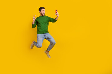 Fototapeta na wymiar Full body photo of video selfie shooting popular blogger show v sign gesture hold smartphone jumping isolated on yellow color background