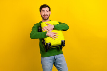 Photo of cheerful man wearing stylish green clothes hold suitbag enjoy summer adventure relax rest isolated on yellow color background