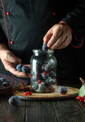 Filling the jar with plums by the hands of the cook. Preparing a sweet drink from fresh plum and sugar on the kitchen table. The process of preserving berries in a jar