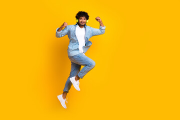 Fototapeta na wymiar Full length photo of excited lucky guy dressed denim jacket rising fists jumping listening songs empty space isolated yellow color background