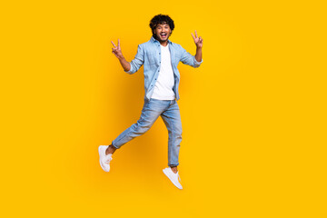 Fototapeta na wymiar Full length photo of positive funny guy dressed denim jacket jumping high showing v-signs isolated yellow color background