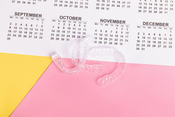 Aligners and calendar on pink and yellow background. Invisible aligners. Duration of treatment
