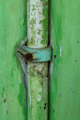 A green pipe clamp that has started to break down due to age against a green wall background