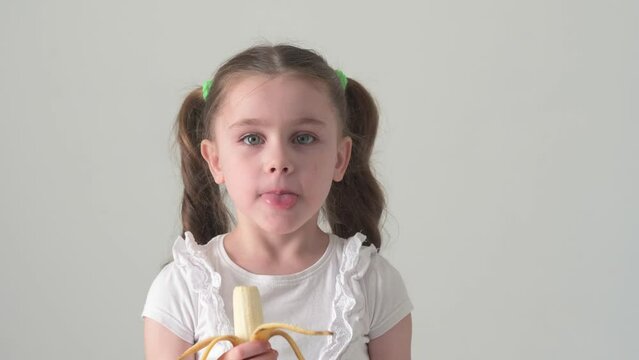 Happy little girl bites and eats banana, fruit and baby.