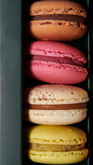 Dark green box with assorted macaroons. Colorful desserts with different filling. Closeup macro photo. Vertical photo.