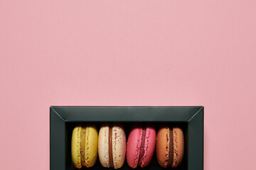 Dark green box with assorted macaroons on the pink background. Colorful desserts with different filling. Free space for text. Horizontal background.