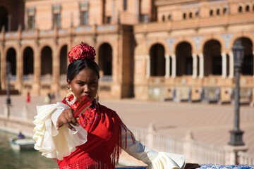 Young black woman dressed as a flamenco gypsy in a famous square in Seville, Spain. She wears a...