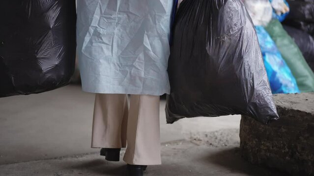Unrecognizable female volunteer placing garbage bags sorting trash on recycling station. Young Caucasian woman in uniform walking with rubbish indoors