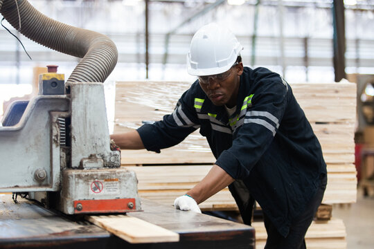 Man American African wearing safety uniform and hard hat working on  electric machines at workshop manufacturing wooden. Male carpenter worker wood warehouse industry.