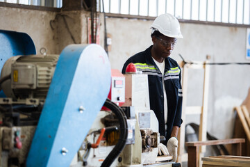Man American African wearing safety uniform and hard hat working on wood sanding electric machines at workshop manufacturing wooden. Male carpenter worker wood warehouse industry.