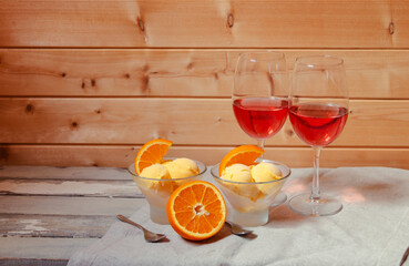 Two glasses of rose wine and orange ice cream in glass bowls on aged wooden table.