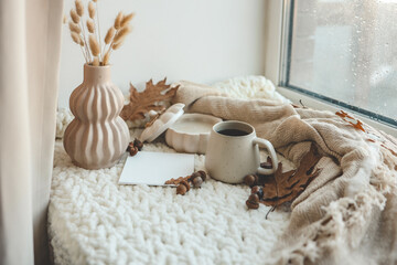 Cup of tea, candle, plaid and leaves in autumn home interior