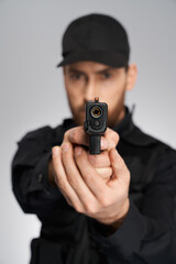 Unrecognizable cop in uniform taking aim, focused on camera indoors. Close up of black weapon, gun, held by blurred police officer silhouette, on gray background. Concept of danger, weapon, target.