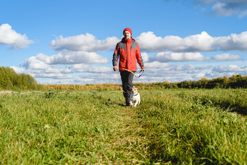 Naklejka na ściany i meble Man and dog on leash walking along path through meadow on bright Fall day