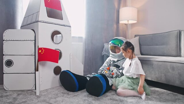 Chinese kids play in the living room at home, a boy in an astronaut costume sitting on the floor with her sister, kids playing with a toy model of the solar system.