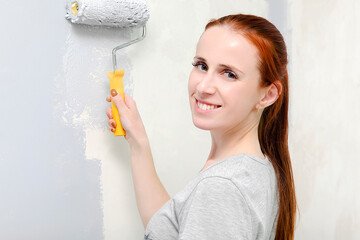 Portrait of young adult girl with red hair,woman painting walls with a gray brush...