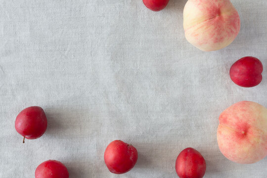 Gray fabric background with fruit frame lined with red plums and pink peaches