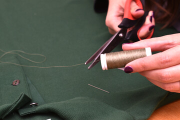 woman sewing with needle and thread a button on a green t-shirt